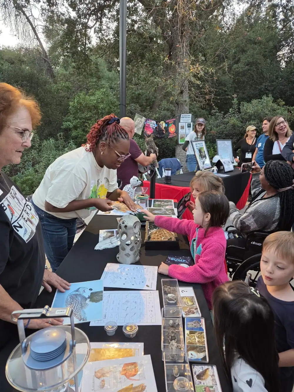 Children gather at an owl-themed activity table while volunteers show them feathers and specimens