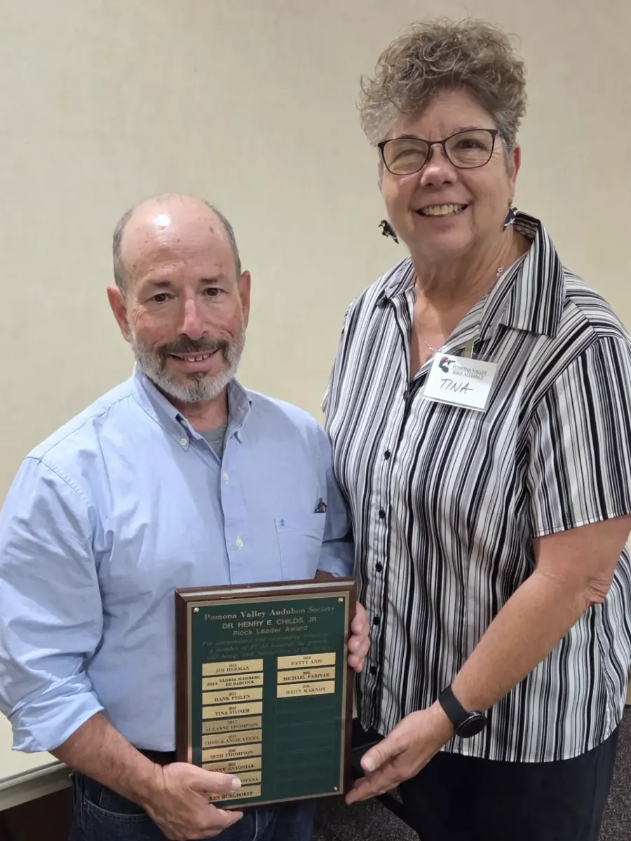 Scott Marnoy smiling and holding the Flock Leader Award plaque, which lists past winners, beside chapter president Tina Stoner.