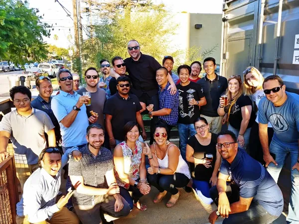A big group of colleagues outside on a sunny day, some holding drinks.